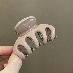 Primer plano de una pinza para el pelo floral en color beige sostenida a mano sobre fondo neutro