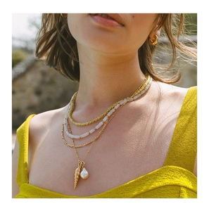 Close-up of layered beaded necklace with shell and pearl charms and gold hoop earrings