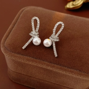 Gros plan de boucles d'oreilles nœud en argent avec zircon et perles sur écrin brun