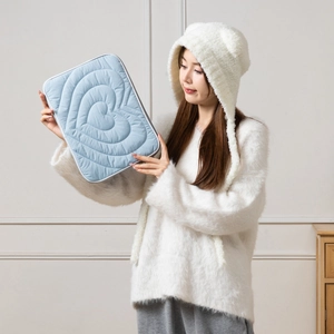 Close-up of light blue heart-quilted tablet sleeve held by a person in a minimalist room