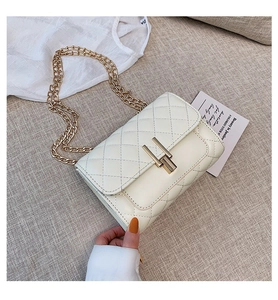 Close-up of a white quilted chain bag with a gold H-shaped clasp on textured fabric