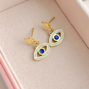 Macro shot of gold star and evil eye drop earrings with blue stone in pink velvet box