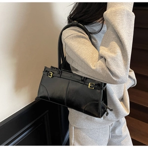 Detailed side view of black glossy shoulder bag with pleats and decorative stitching