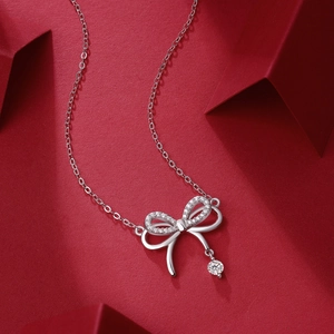 Detailed view of silver bowknot pendant necklace with crystals on red background