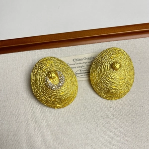 Détail macro de boucle d'oreille tressée dorée avec strass et texture métallique
