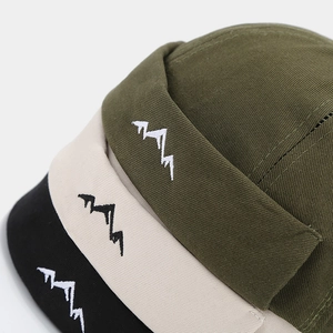 Detailed close-up of mountain embroidery on cotton docker hats in green, beige, and black