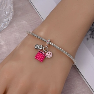 Close-up of silver snake chain bracelet featuring pink enamel knitting charms on wrist