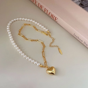 Detail of asymmetrical pearl and gold paperclip chain necklace with a heart pendant