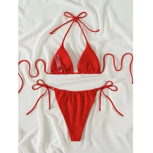 Flat lay detail of red triangle bikini top and tie-side bottom on white fabric