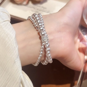 Macro shot of three-layer pearl bracelet with zircon cylinder buckle on woman's wrist