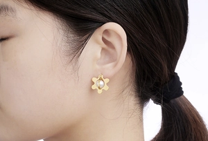 Detail of gold flower earrings with white pearl center worn by a female model