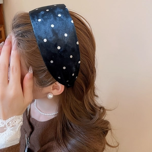 Close-up of a wide vintage headband with white polka dots on dark velvet fabric