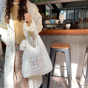 Close-up of white plush tote bag with cartoon embroidery and mini bear charm detail