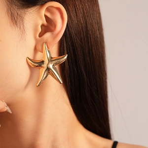 Detailed view of large gold starfish earrings with glossy metallic finish on model