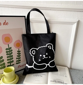 Close-up of black Oxford tote bag with white cartoon bear print on a desk setting