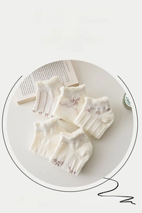 Close-up of five white cotton ankle socks with ruffles and bows in a soft lifestyle set