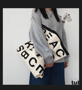 Detailed view of cream canvas tote bag with bold black letters on a model