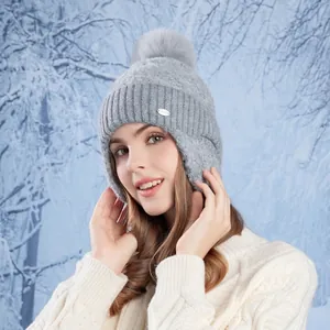 Winter grey cable knit ear flap beanie hat with faux fur pom-pom against snowy forest