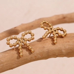 Close-up of 18K gold plated bow earrings made of small beads on a wooden branch