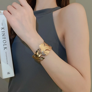 Detailed view of a gold leaf-shaped open cuff bracelet worn on a wrist next to a book