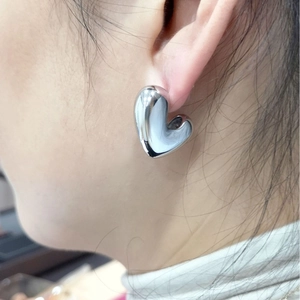 Polished silver heart stud earrings shown from a side view perspective on a model