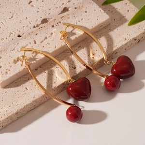 Detail view of gold cherry earrings with red heart and round resin beads on stone background