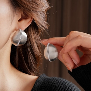 Close-up of a silver brushed teardrop earring with pearl accents worn by a model