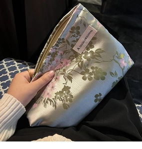 Detail of silver silk makeup bag with pink floral patterns and a woven logo label