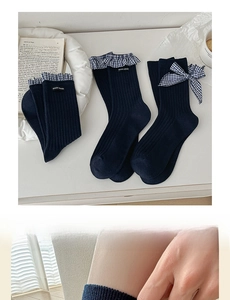 Close-up of navy blue mid-calf socks with plaid lace trim and bow on cream background