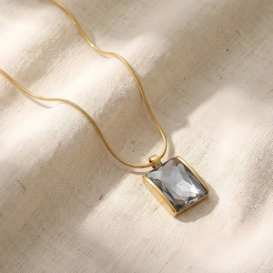 Detail of a rectangular grey glass pendant on an 18K gold-plated snake chain necklace