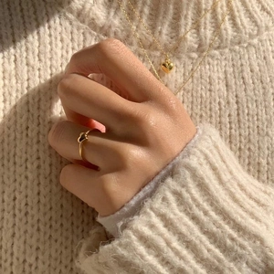 Detail of golden heart ring and necklaces worn over a beige textured knit sweater