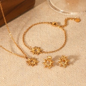Detailed set of gold sunburst necklace, bracelet and earrings on textured fabric background