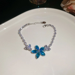 Silver bracelet featuring a blue rhinestone flower and sparkling crystals on white ceramic