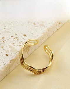 Détail d'une bague vague en acier inoxydable plaqué or 18k sur fond de pierre texturé
