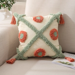 Detail of bohemian tufted cushion cover with green diamond patterns and orange tassels