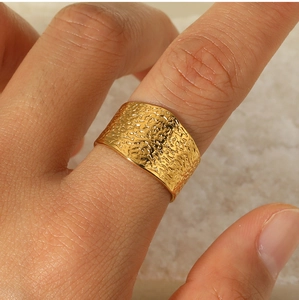 Macro shot of wide golden C-shape stainless steel ring with unique hammered metal texture