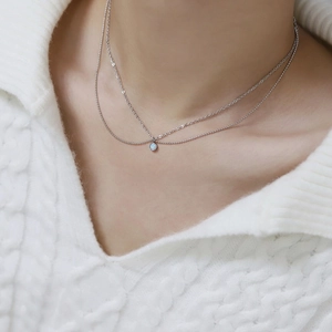 Double-layered silver titanium necklace with round light blue opal stone on white sweater