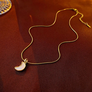 Detail of a crescent moon pendant necklace with white shell inlay on a gold snake chain
