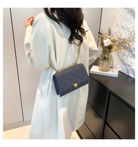 Detail of dark blue quilted crossbody bag with gold chain strap on a white coat