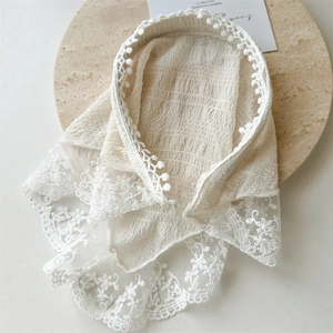 Detail of beige seersucker lace headband with floral embroidery and pom-pom trim on wood