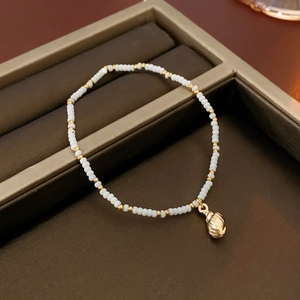 Detail of bohemian shell bead bracelet with gold pendants on a dark jewelry tray