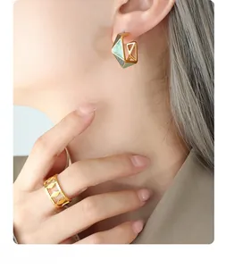 Detailed view of geometric gold earrings with green enamel and hollow rhombus ring on model