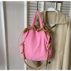 Borsa a secchiello in nylon rosa con coulisse marrone e manico intrecciato su un cappotto
