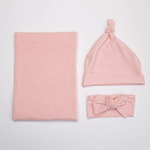 Flat lay of pink newborn set including a swaddle blanket, knot hat, and bow headband