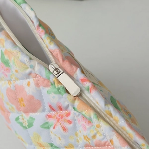 Macro detail of diamond-quilted floral makeup bag featuring a silver metal zipper