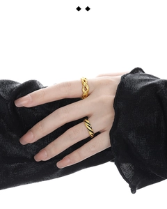 Detail of twisted gold ring and black helix band design worn by a model on white backdrop
