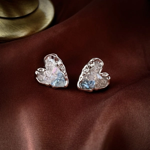 Détail de boucles d'oreilles cœur argentées avec cristaux bleus sur soie sombre