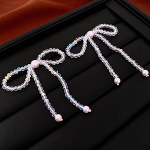 Macro detail of bead-woven bow earrings with dangling imitation pearl tassels