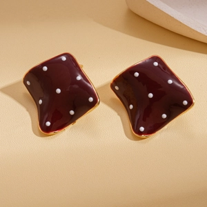 Macro detail of dark red enamel square stud earrings with white polka dots and gold edges