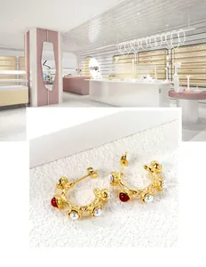 Detail of golden C-shaped hammered earrings with white pearls and red gemstone